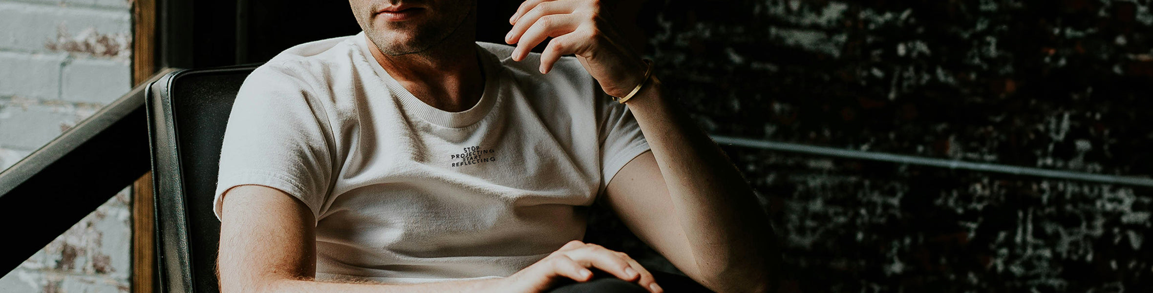 Man contemplating in a relaxed pose with a thoughtful expression wearing a casual white t-shirt with text, representing Maple and Rhine's lifestyle brand.